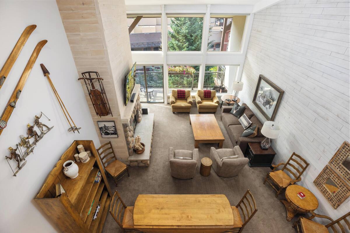 A spacious living room with a high ceiling, large windows, a dining area with a wooden table, and a cozy seating arrangement.