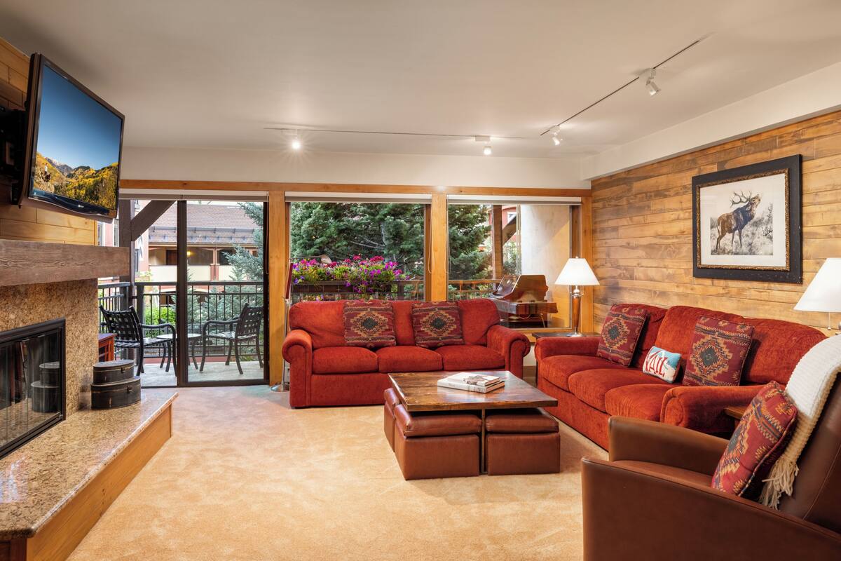 A living room with a fireplace, red sofas, a coffee table, and a television mounted on the wall.