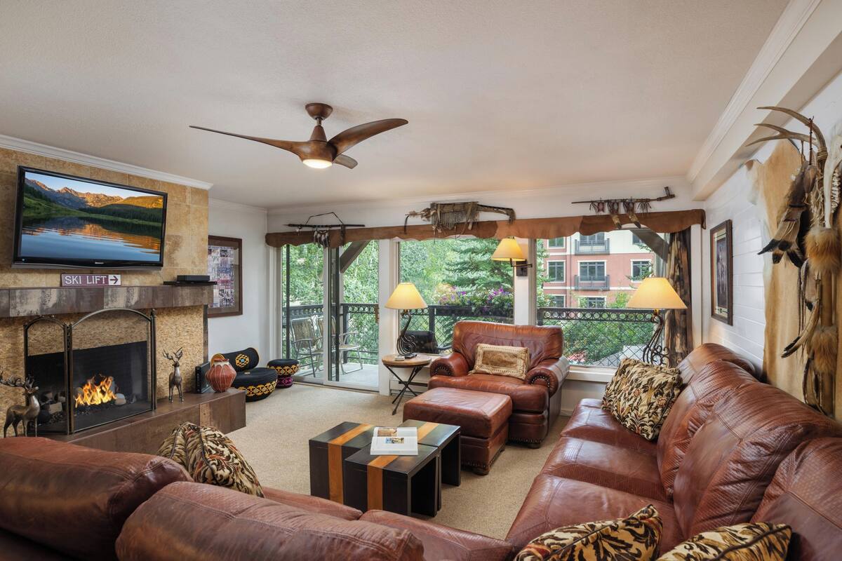 A living room with a fireplace, leather furniture, a ceiling fan, and a television.
