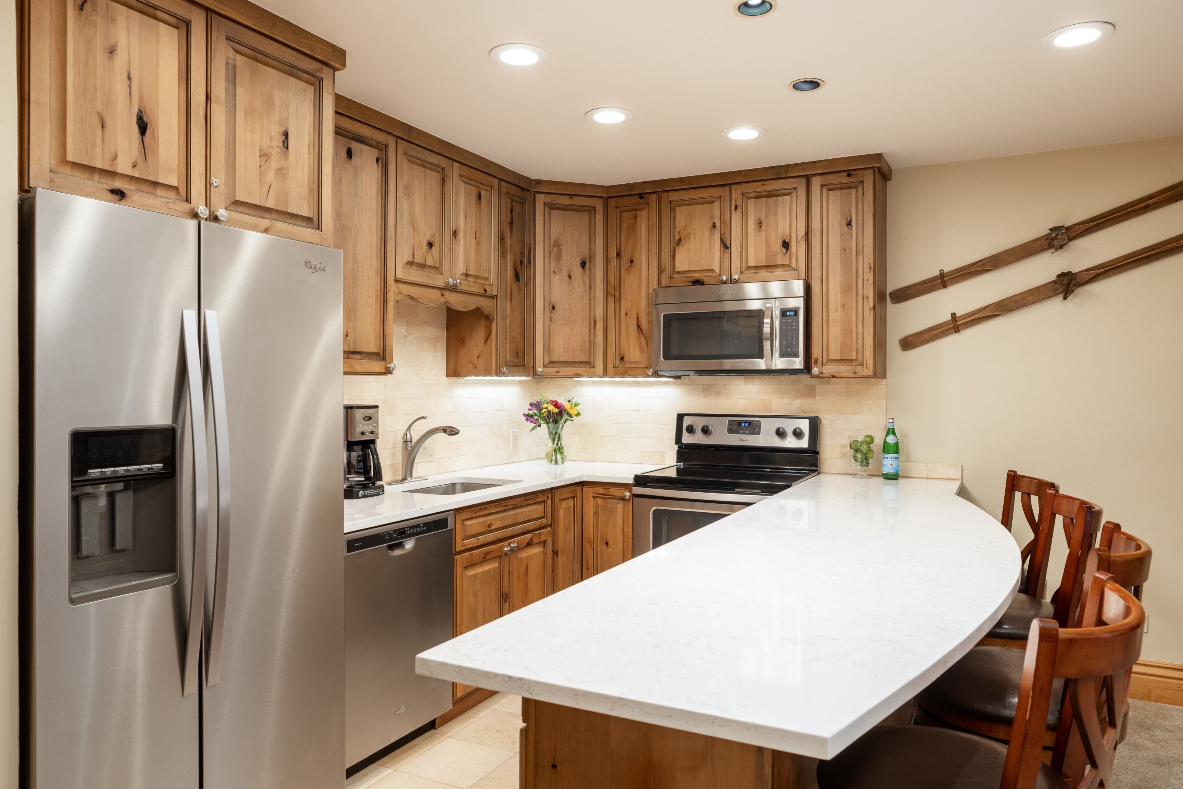 A kitchen with wooden cabinets, stainless steel appliances, a white countertop, and a dining area with wooden chairs.