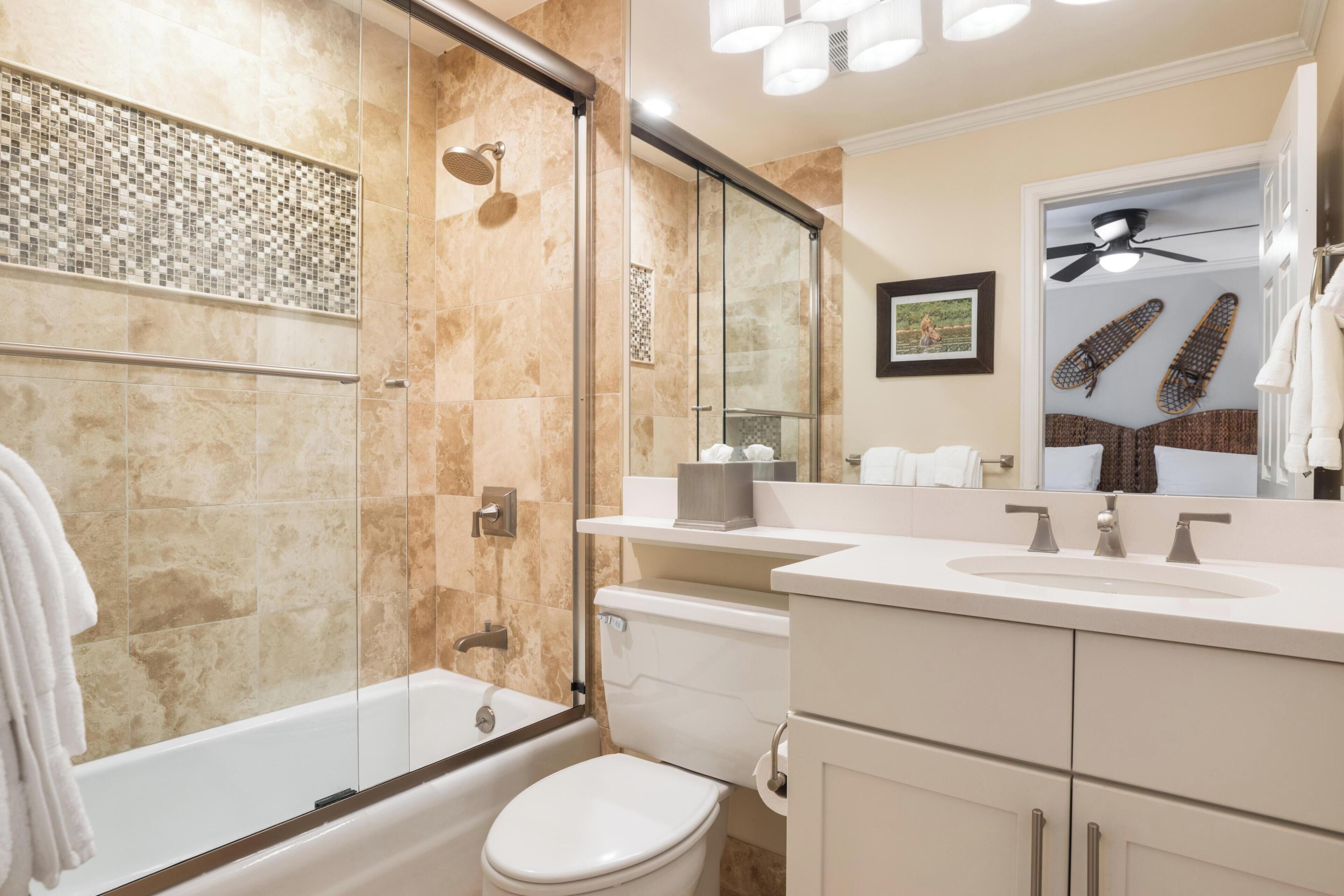 A modern bathroom with a glass-enclosed shower, a white toilet, and a vanity with a mirror.