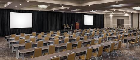 A conference room with rows of tables and chairs, a large screen, and a podium.
