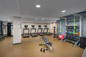 Un gimnasio con cintas de correr, una banca, mancuernas y una estructura con pesas rusas.