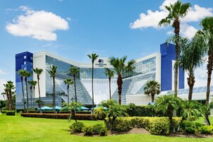 A modern hotel with a glass facade, palm trees, and a clear blue sky.