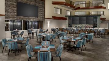 A spacious dining area with multiple tables and chairs, a bar area with a counter and stools, and a large screen on the wall.