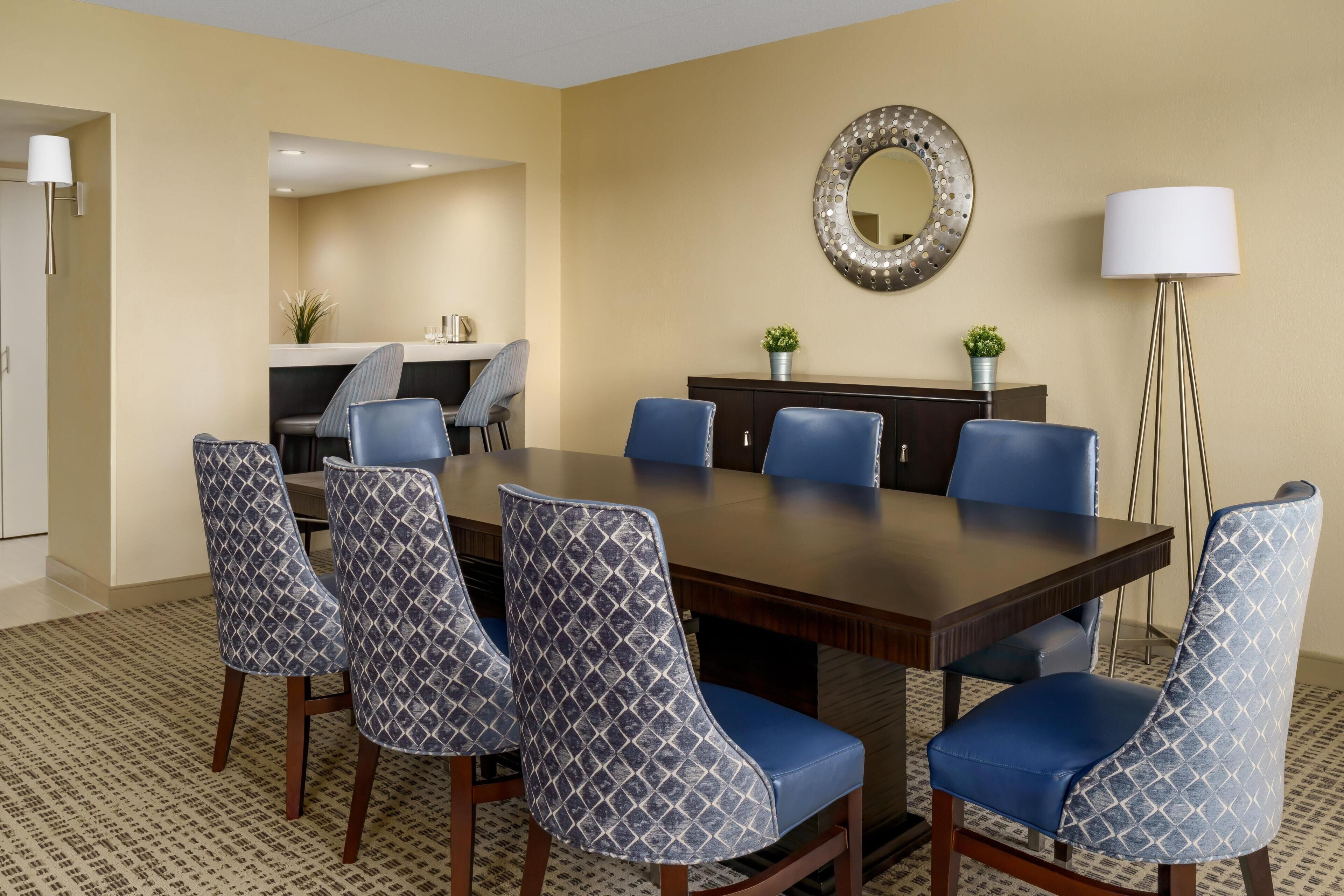 A conference room with a large table, six chairs, a round mirror, and a floor lamp.