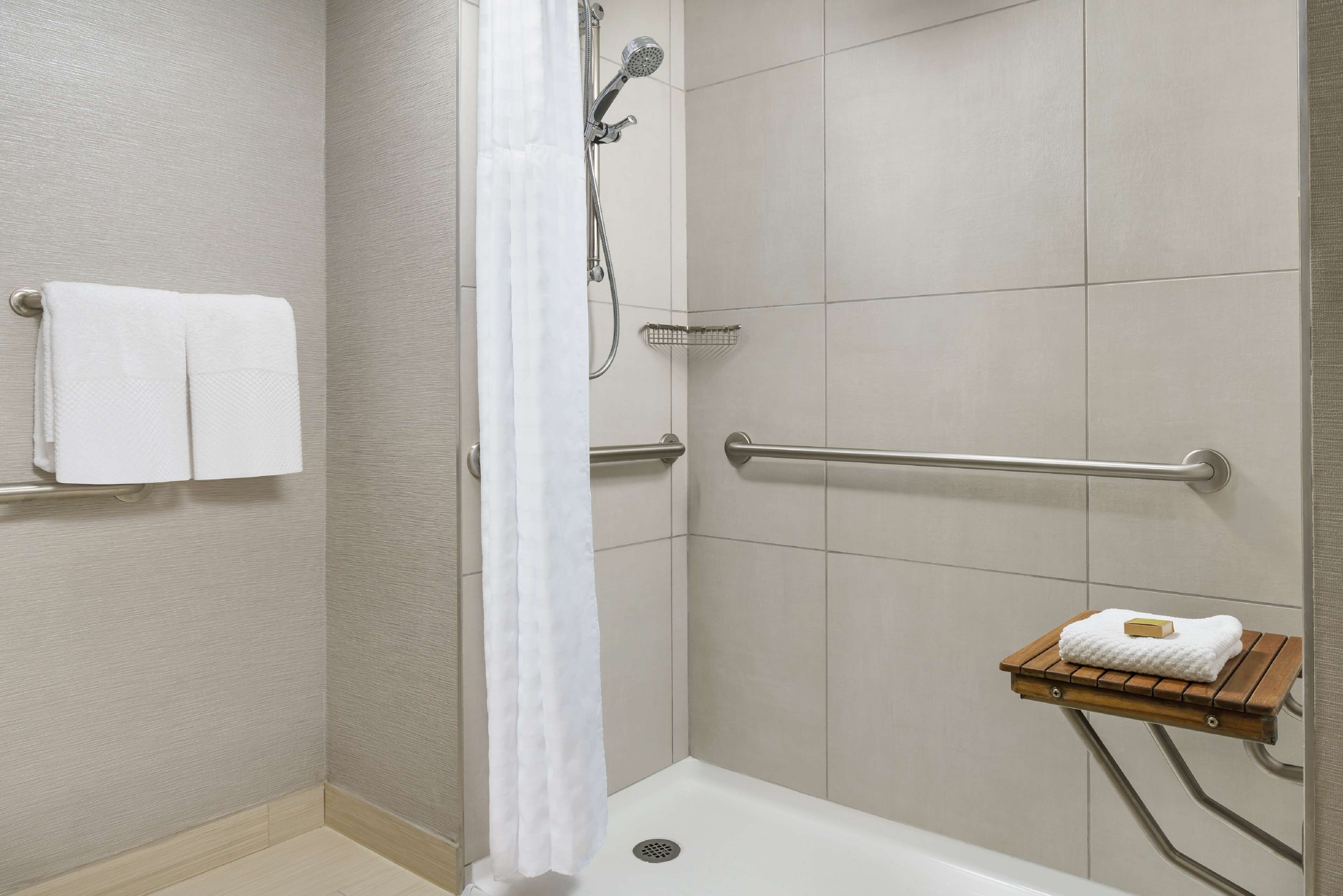 A shower area with a grab bar, a towel rack with two towels, and a wooden shelf with a towel.