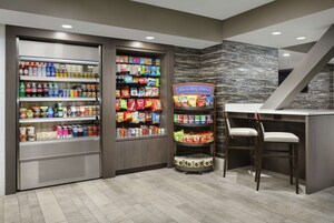 A snack bar with shelves stocked with various snacks and beverages, a seating area with two chairs, and a stone-patterned wall.