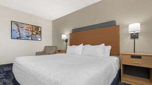 A hotel room with a large bed, a headboard, two bedside tables with lamps, a chair, and a painting on the wall.