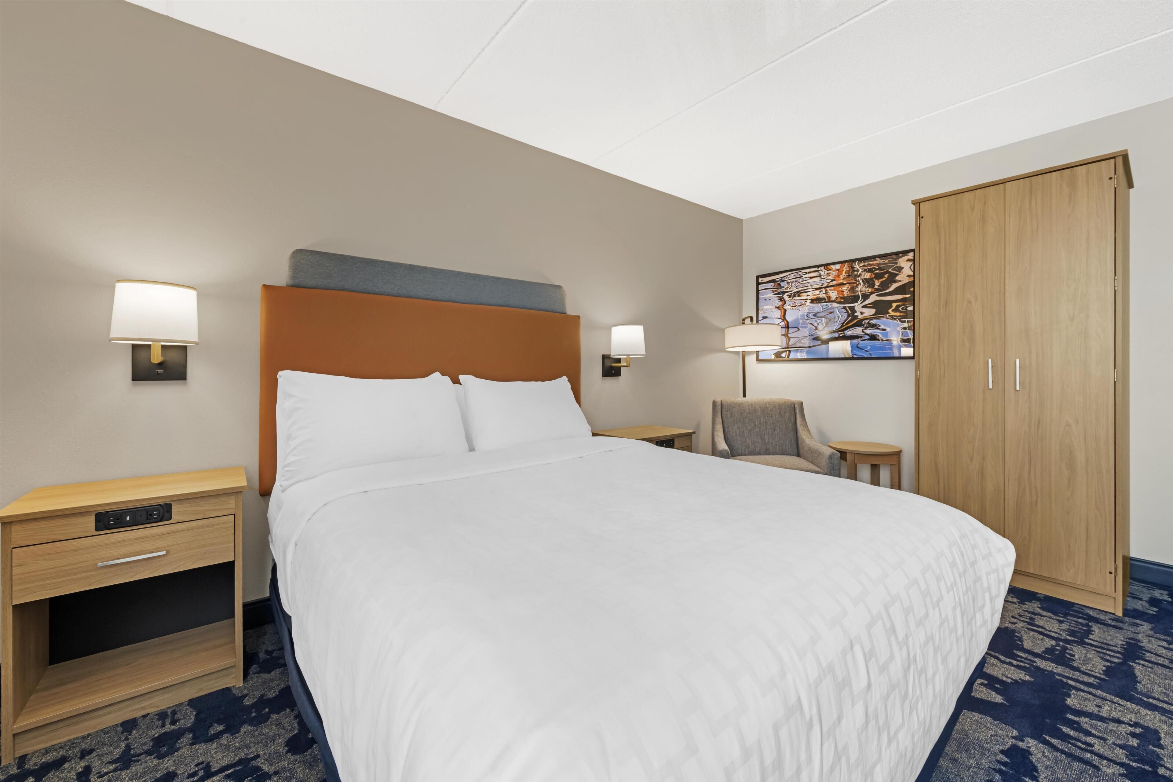 Une chambre d’hôtel avec un grand lit, des tables de chevet, une armoire et deux lampes fixées au mur.