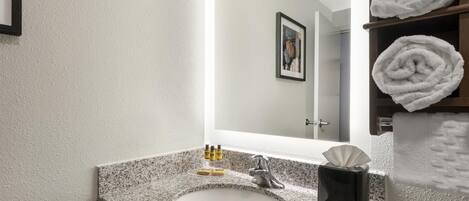 Un baño con lavamanos de encimera de granito, un espejo, un cuadro en la pared y un perchero con toallas dobladas.
