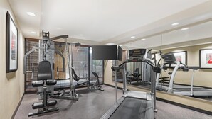 A gym with a treadmill, weight machines, and a mirrored wall.