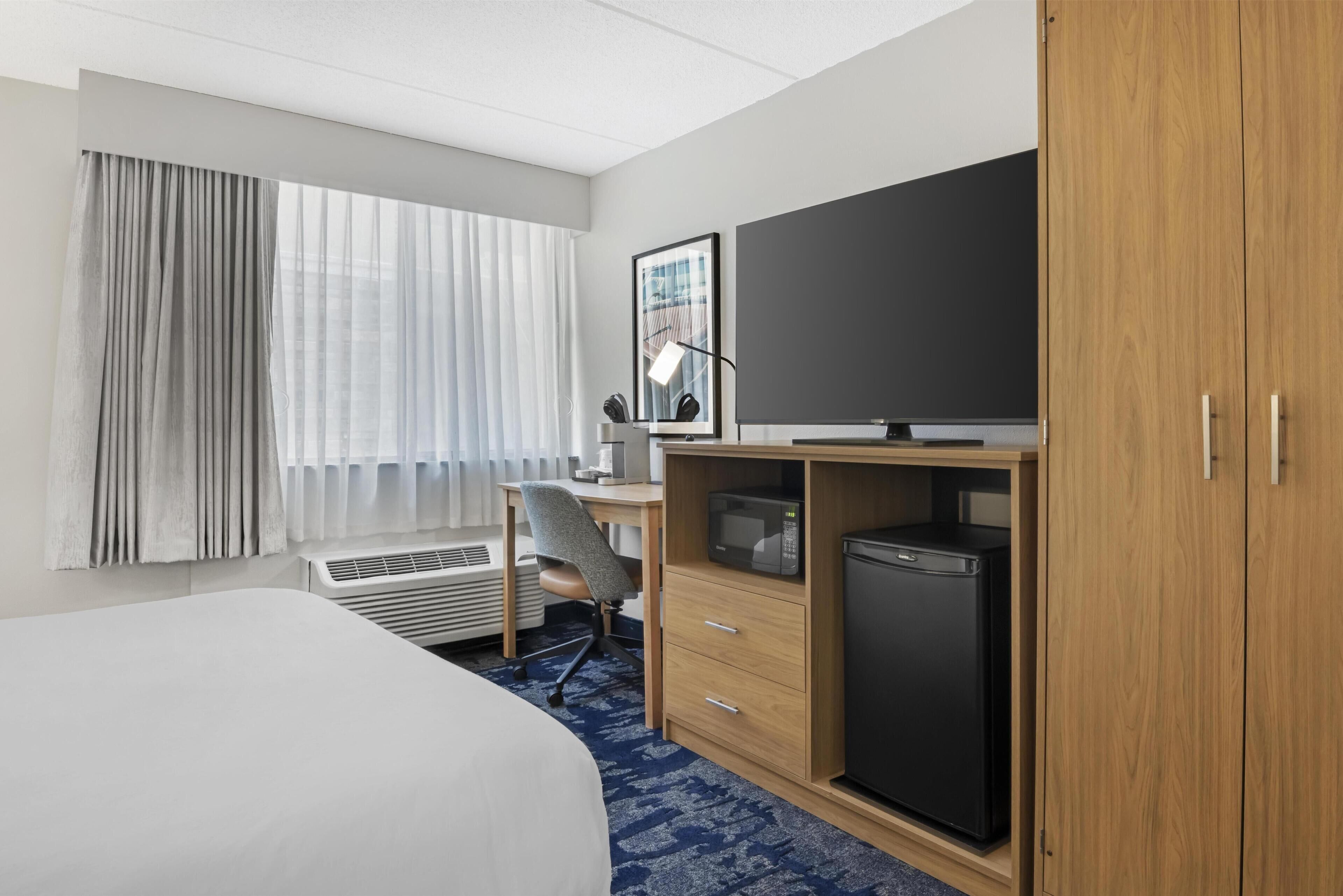 A hotel room with a bed, a desk with a chair, a television, a microwave, and a refrigerator.