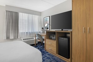 Ein Hotelzimmer mit einem Bett, einem Schreibtisch mit Stuhl, einem Fernseher, einer Mikrowelle und einem Kühlschrank.