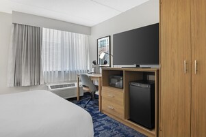 Habitación de hotel con cama, escritorio con silla, televisión, microondas y refrigerador.