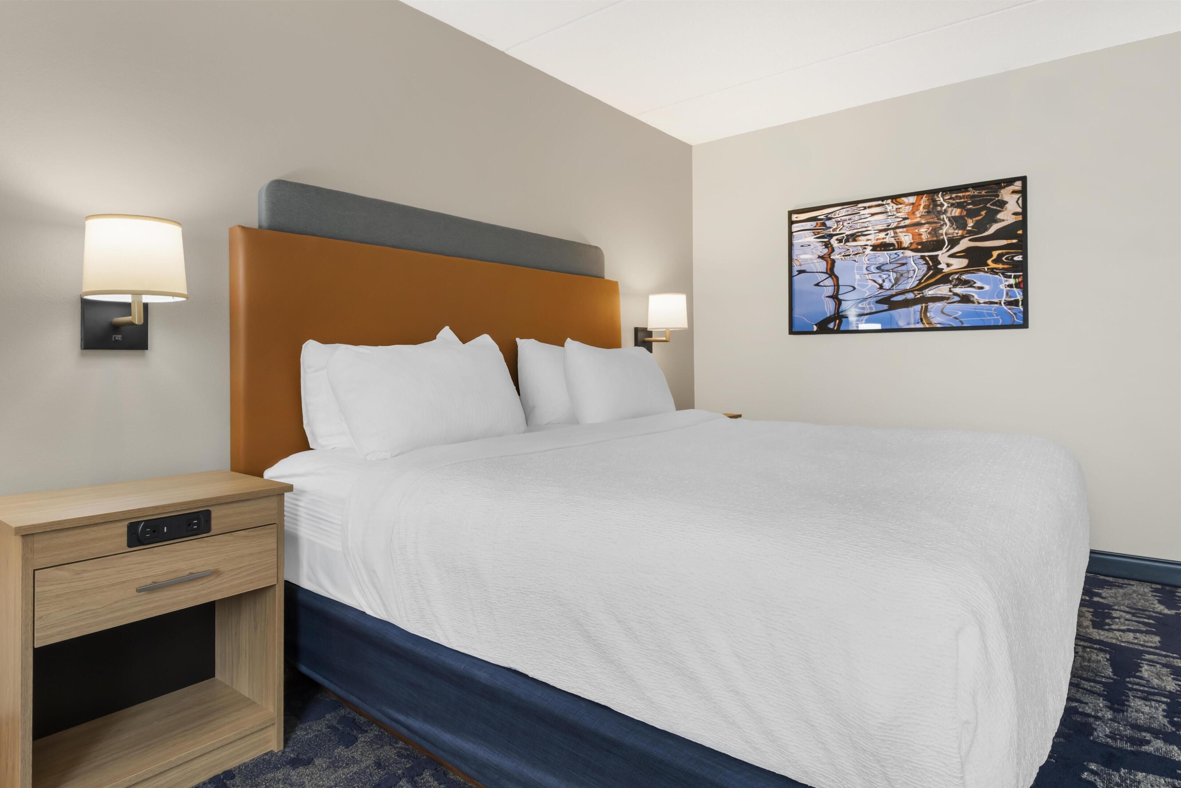 Een hotelkamer met een bed, nachtkastjes, wandlampen en een ingelijst kunstwerk aan de muur.