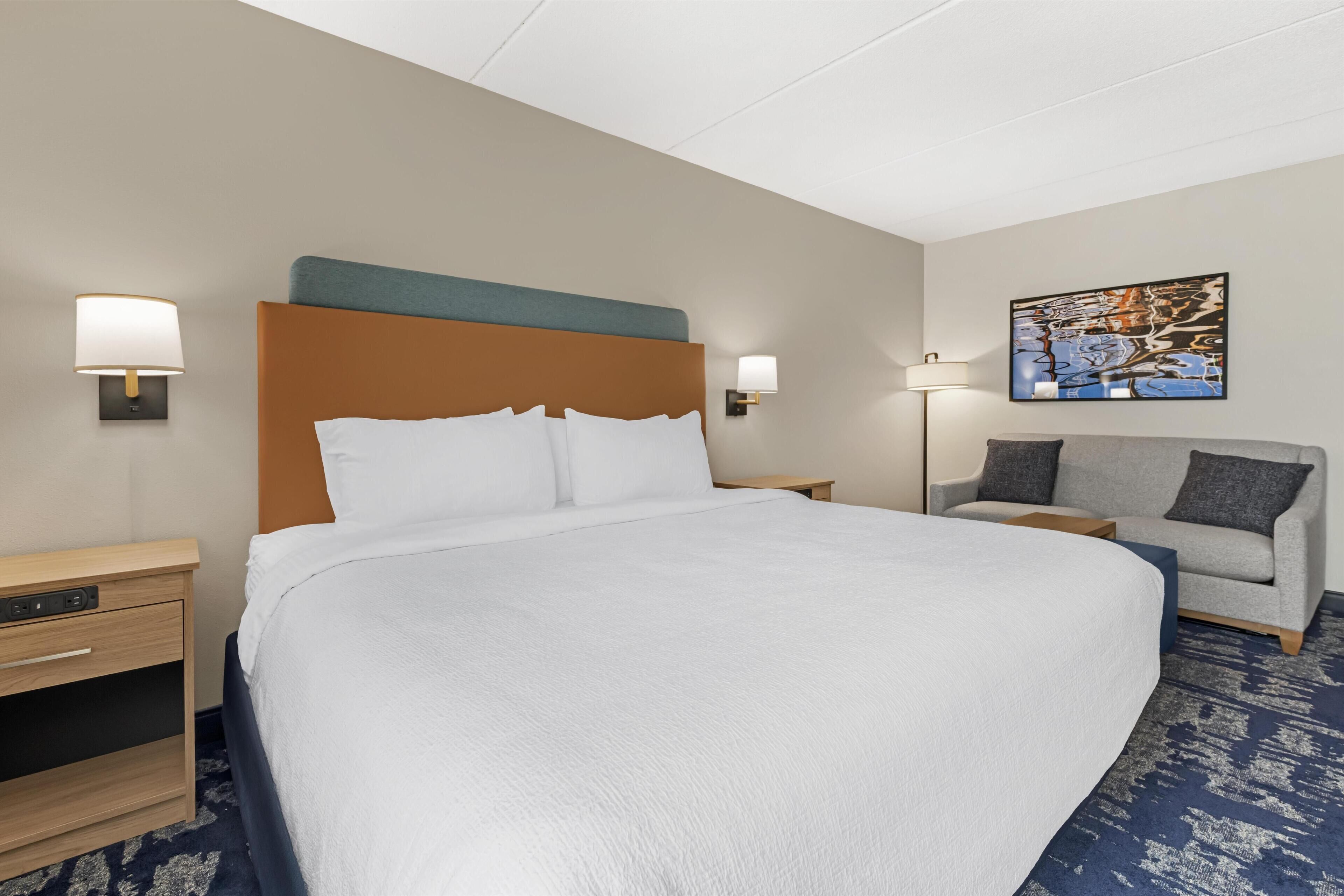A hotel room with a large bed, two bedside tables, a desk, a sofa, and a painting on the wall.
