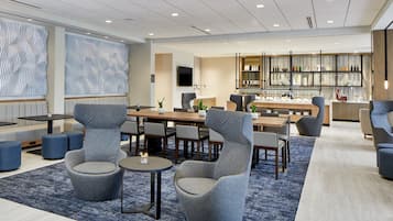 Un hall d’hôtel moderne avec un espace salon central, un bar et une présentation de bouteilles.