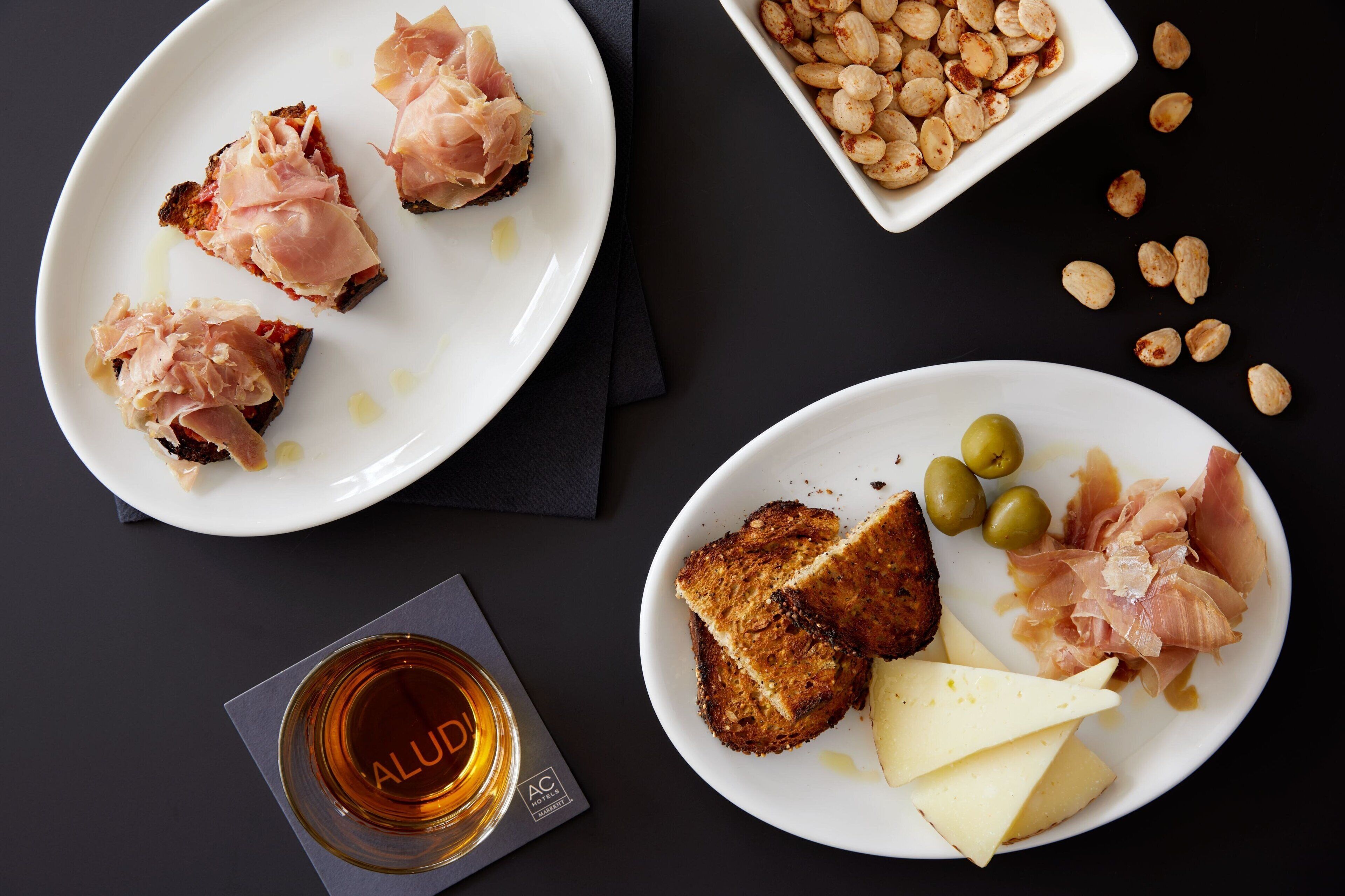 Una mesa con platos de comida que incluyen tostadas, queso, aceitunas y embutidos.