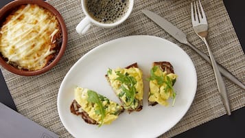 A plate with scrambled eggs and greens, a bowl of baked dish, a croissant, and breakfast utensils on a table.