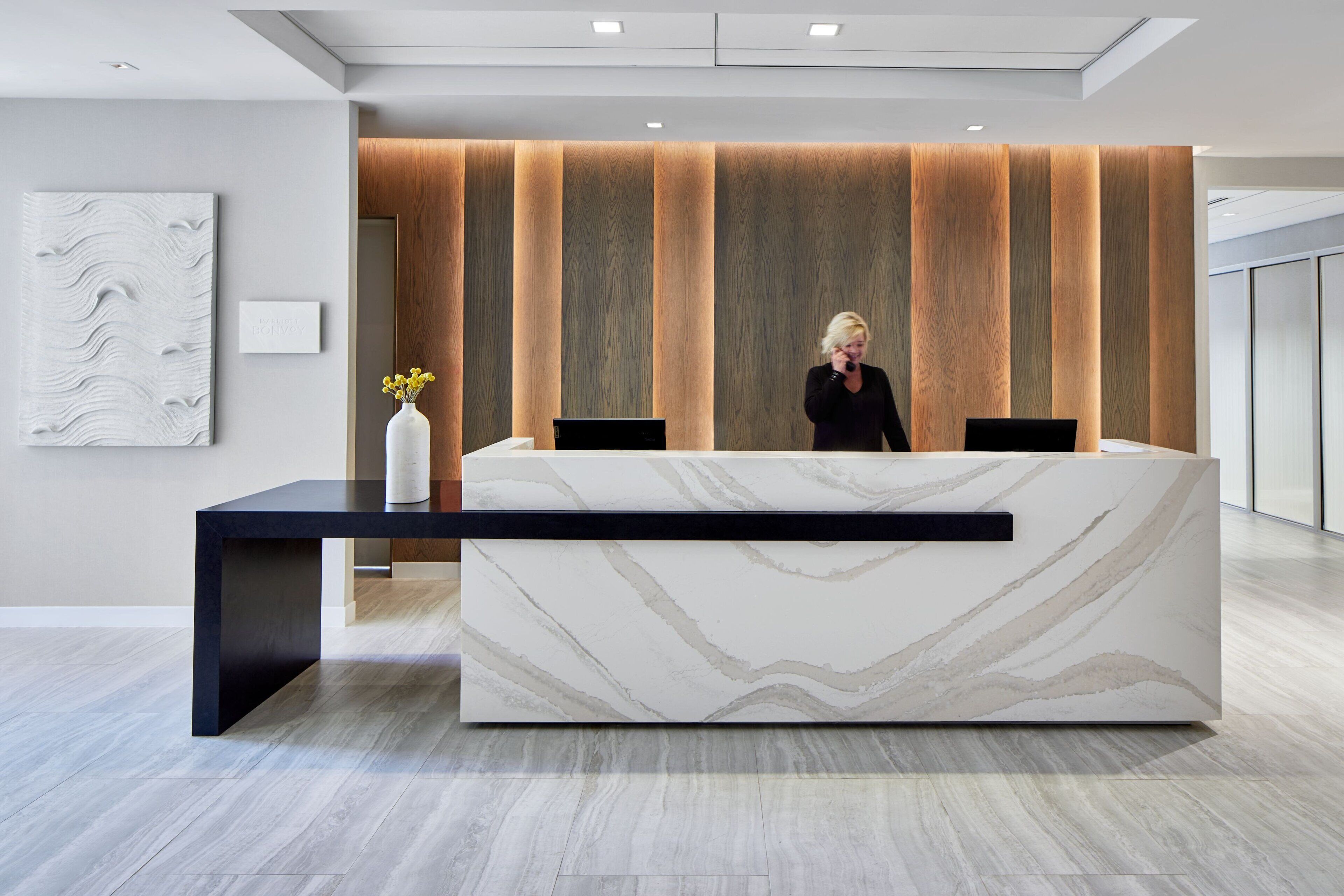 A modern reception desk with a marble top, a black base, and a wooden accent wall.