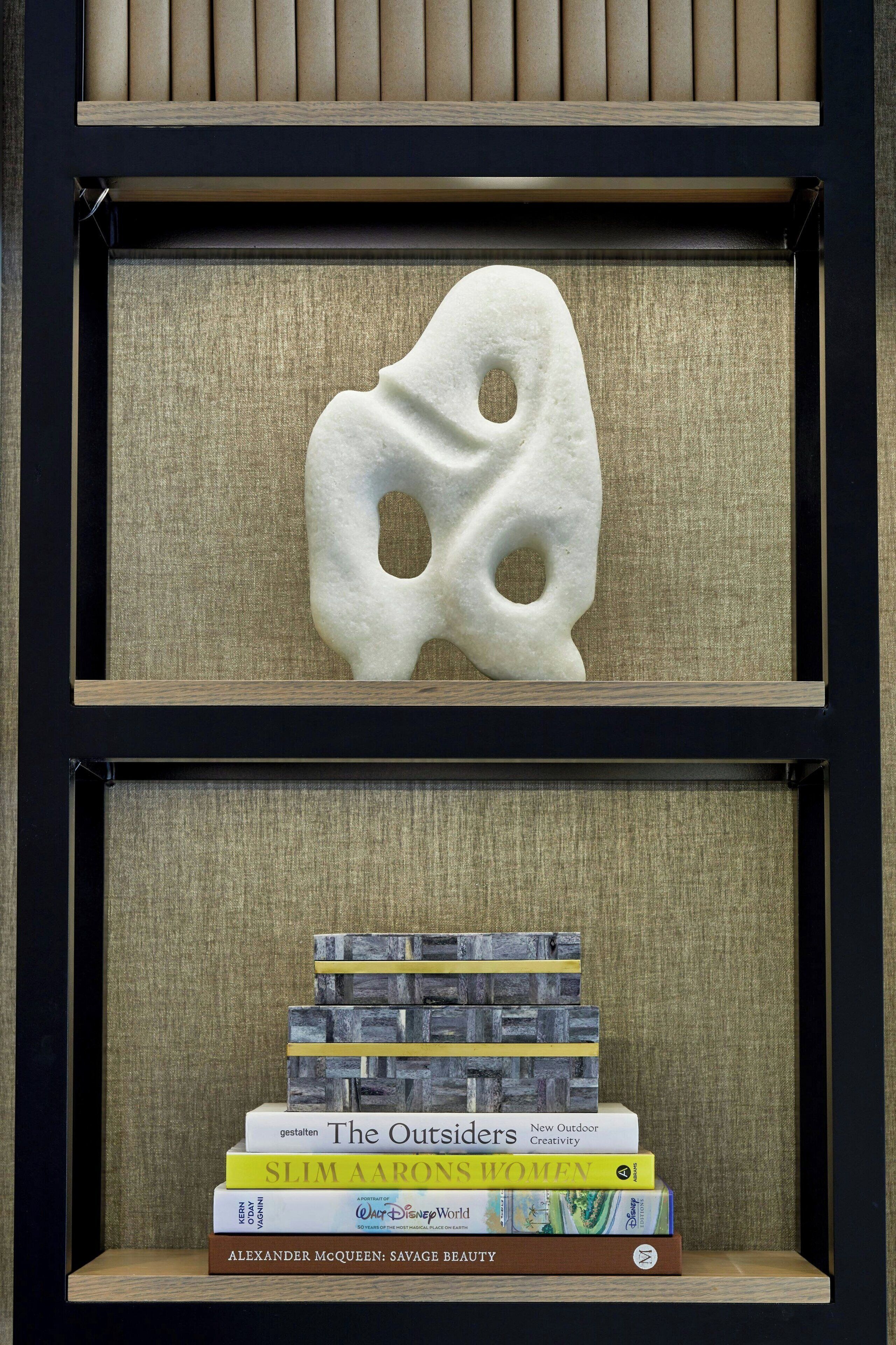 A bookshelf with a unique white sculpture and a stack of books.