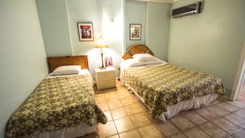 Une chambre avec deux lits simples, une table de chevet avec une lampe et un climatiseur fixé au mur.