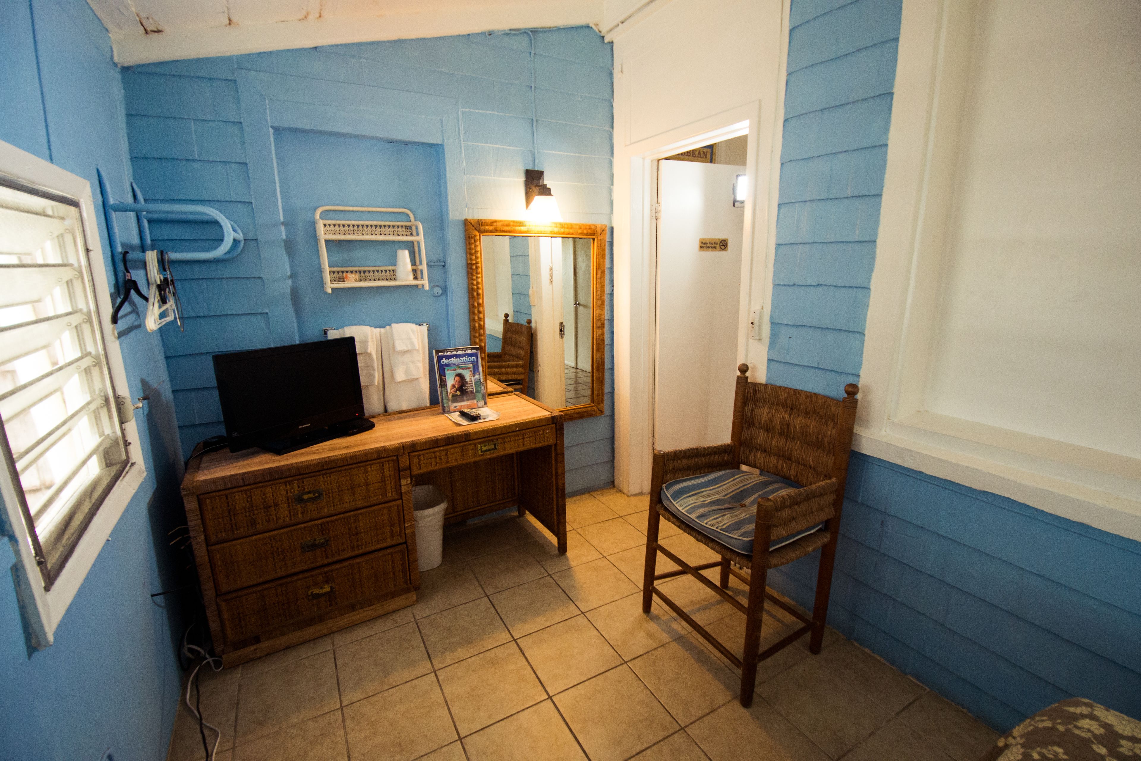 Een badkamer met blauwe wanden, een houten wastafelmeubel, een stoel, een spiegel en een toilet.