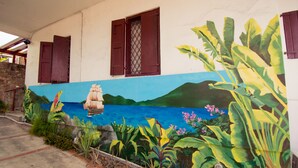 Un bâtiment orné d’une fresque représentant un navire sur une mer bleue, entouré de plantes tropicales.