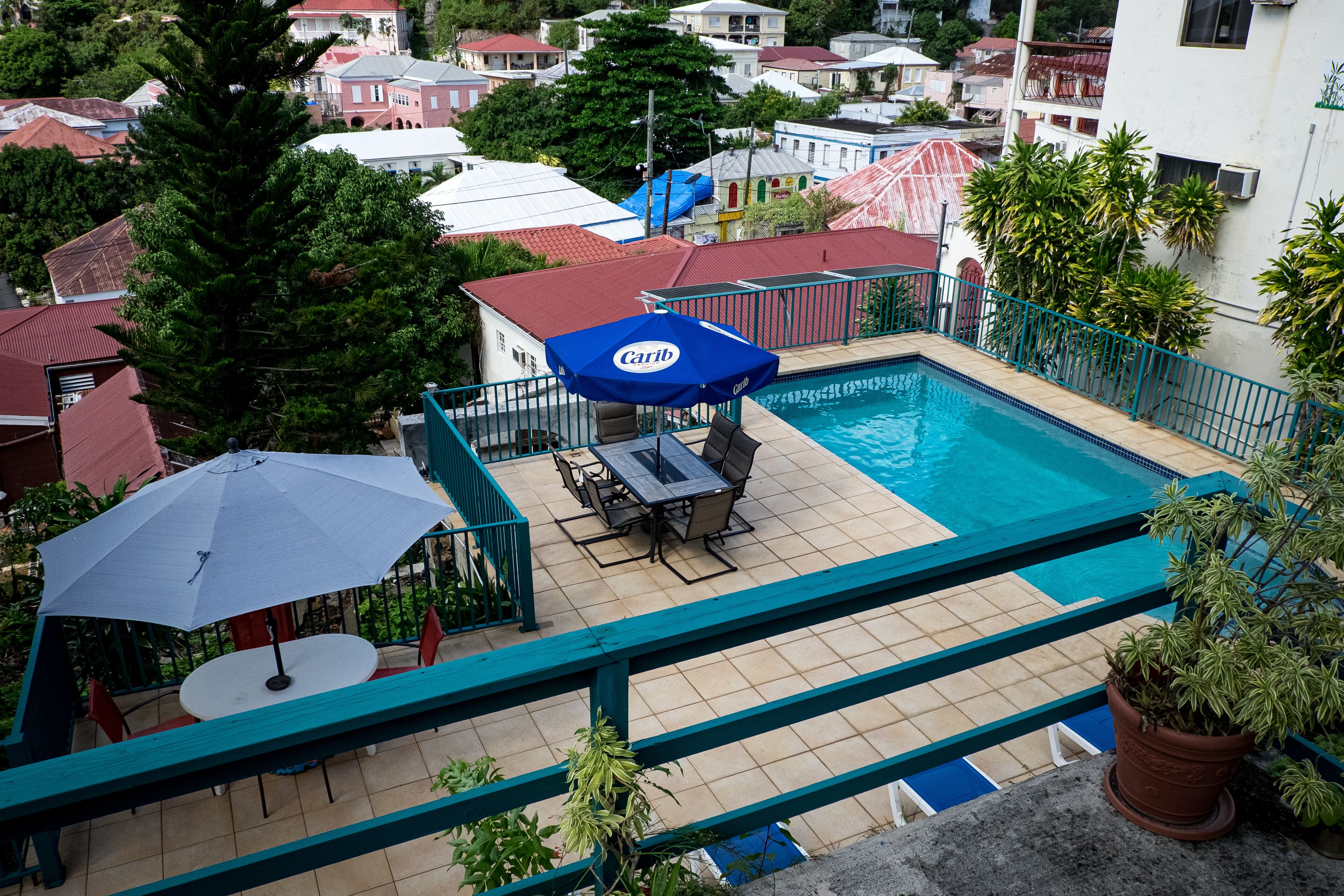 Un espace piscine aménagé sur le toit, avec un parasol bleu, une table et des chaises, et un pot de fleurs.