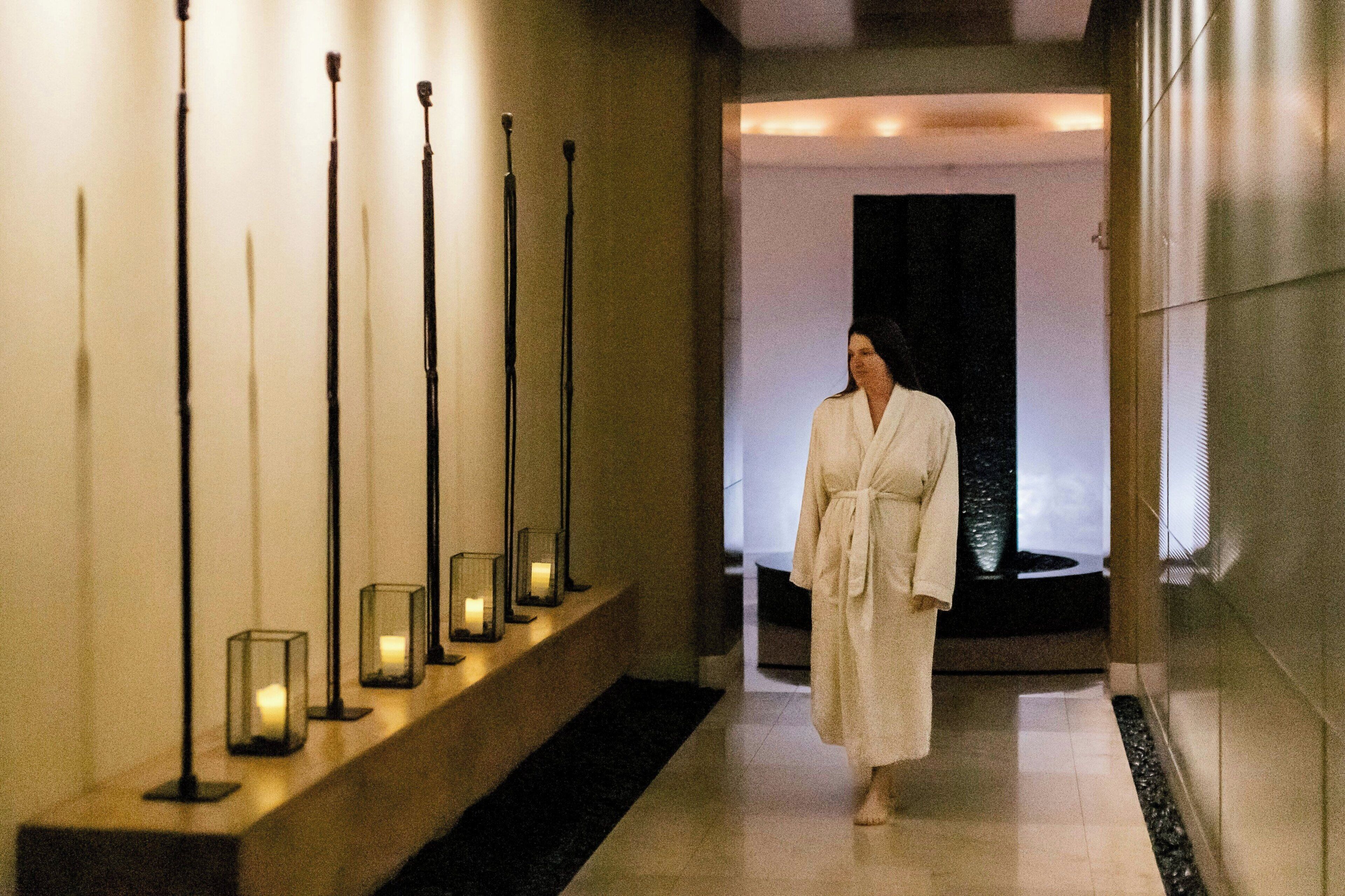 Un pasillo con varios candelabros y una persona con bata caminando.