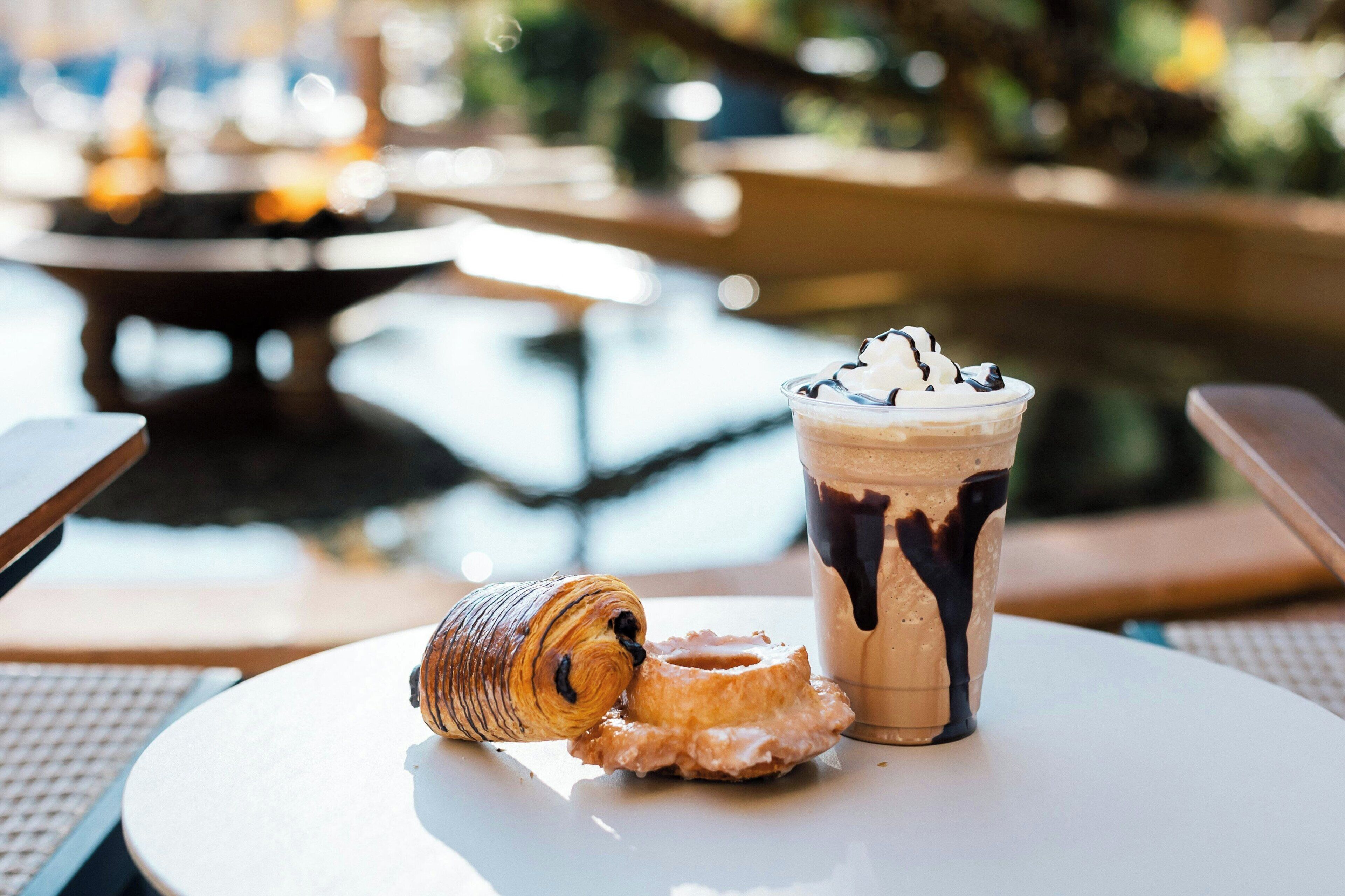 Una mesa con un pastel, una bebida con crema batida y sirope de chocolate, y una rosquilla.