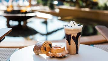 Una mesa con un pastel, una bebida con crema batida y sirope de chocolate, y una rosquilla.