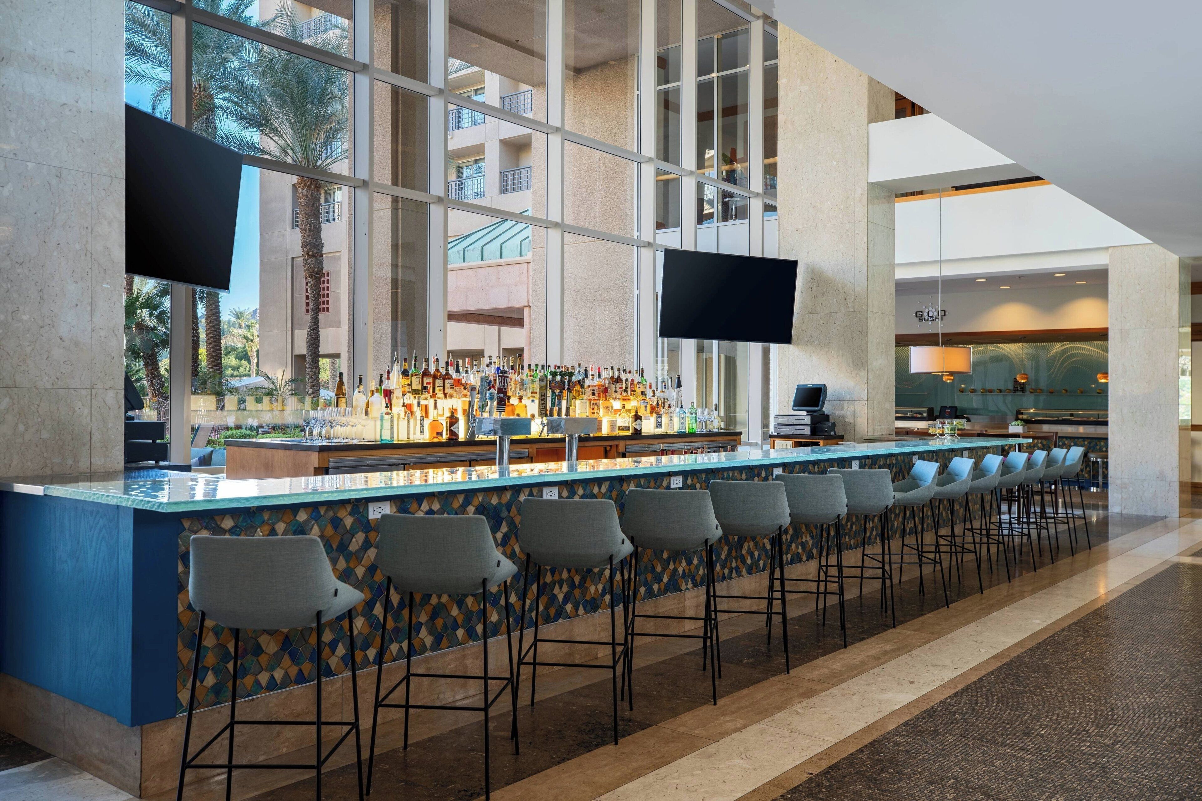 A modern bar area with a long counter, multiple bar stools, and a view of the outdoor balcony.