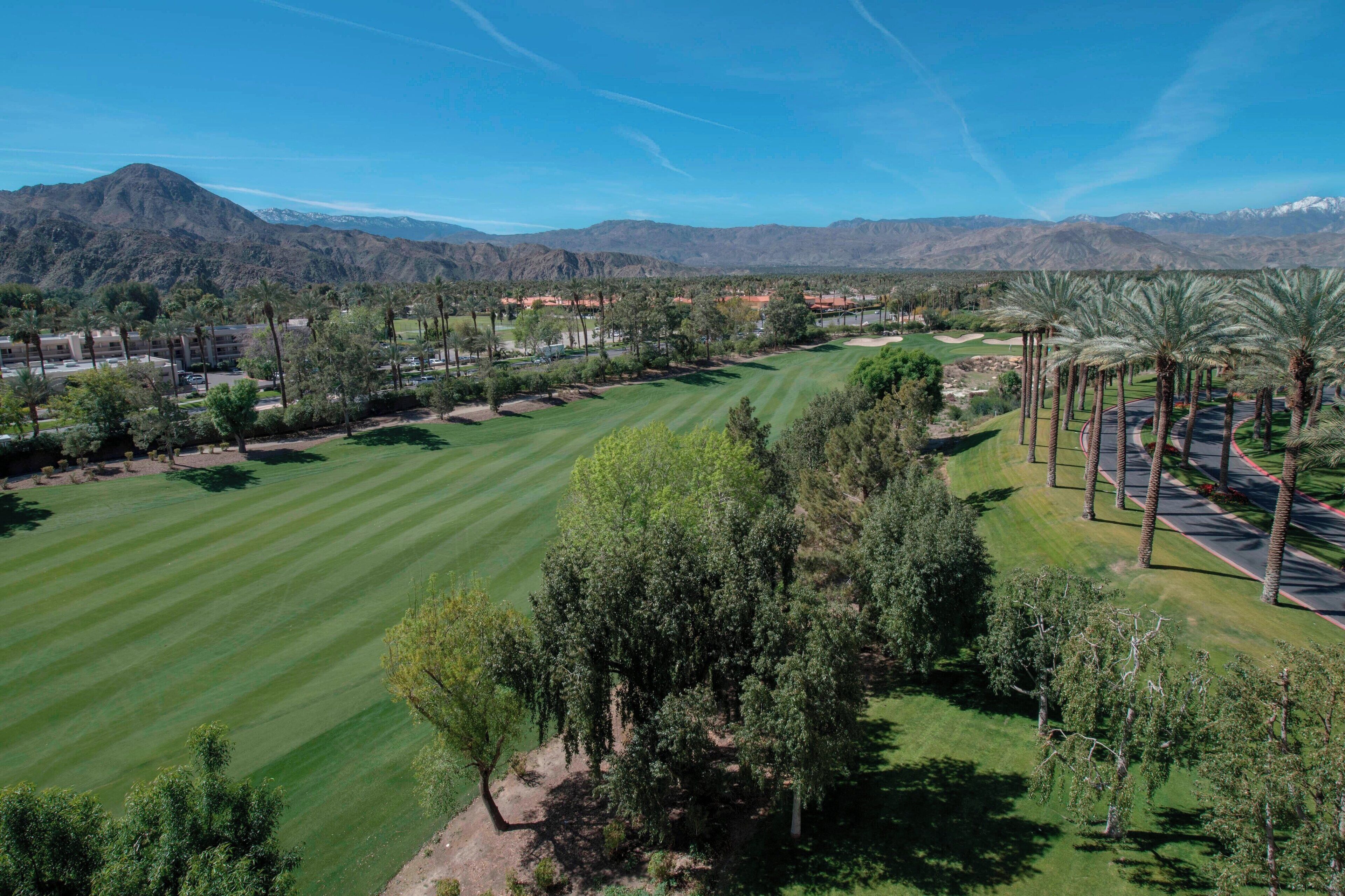 Un parcours de golf offrant une vue dégagée sur le paysage environnant, notamment sur les montagnes, et comprenant un espace de stationnement agrémenté de palmiers.