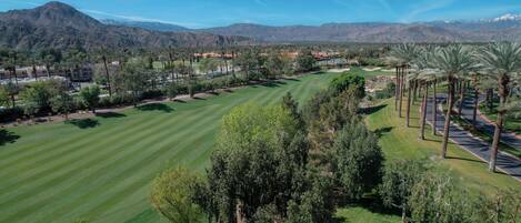 Un parcours de golf offrant une vue dégagée sur le paysage environnant, notamment sur les montagnes, et comprenant un espace de stationnement agrémenté de palmiers.