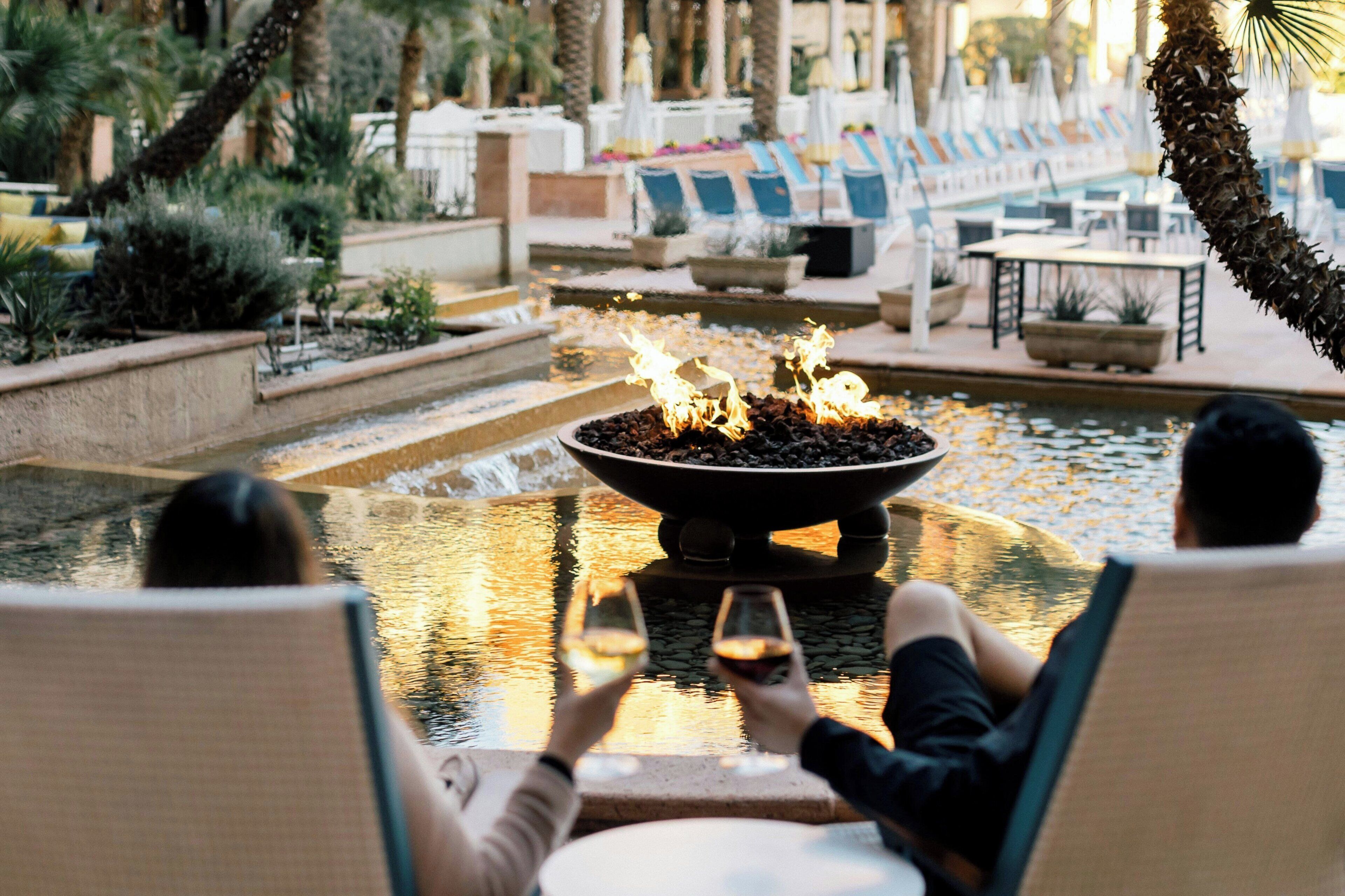 Un couple se détend au bord d’une piscine agrémentée d’un foyer, de chaises longues et d’une fontaine.
