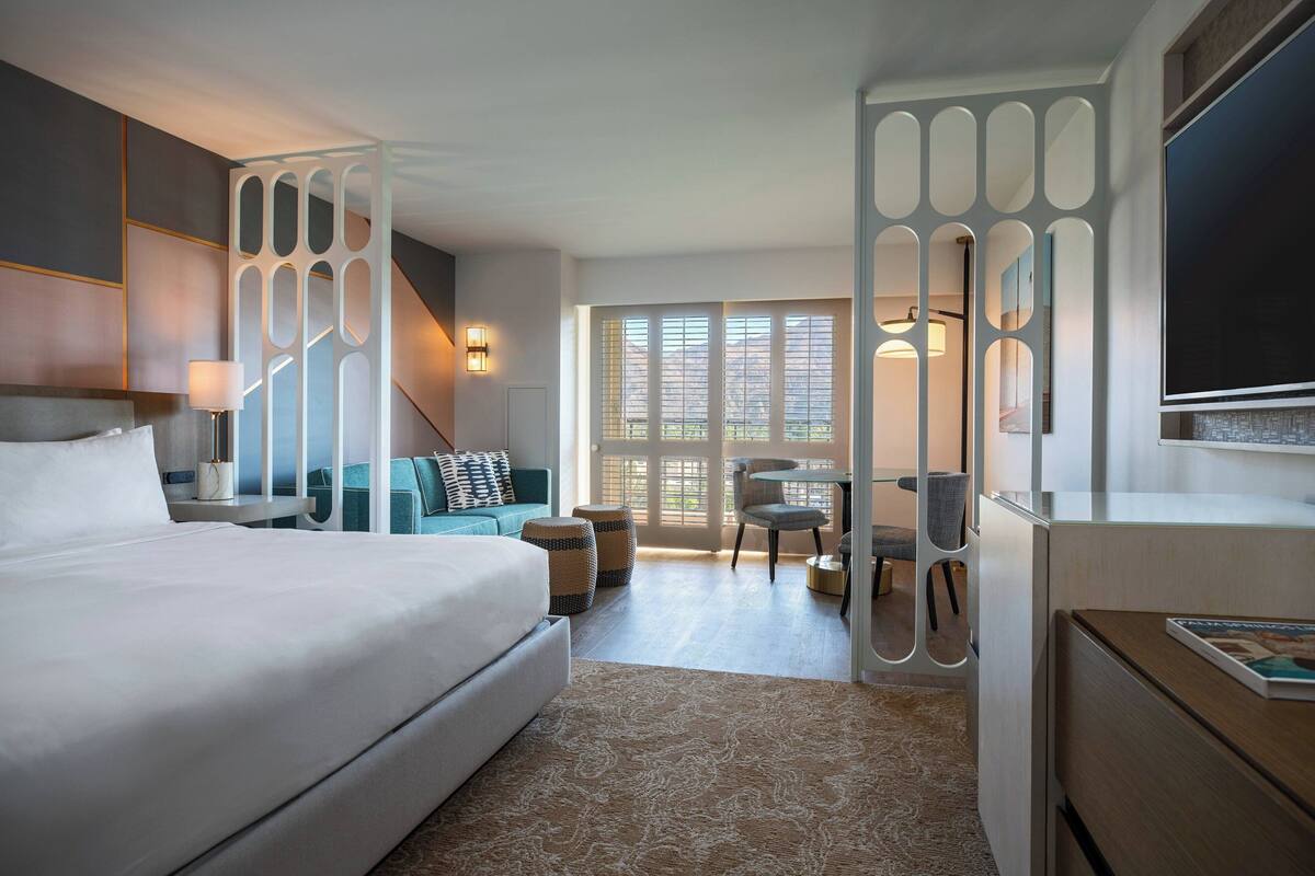 A modern hotel room with a large bed, a seating area with a sofa and chairs, a small table, and a TV.