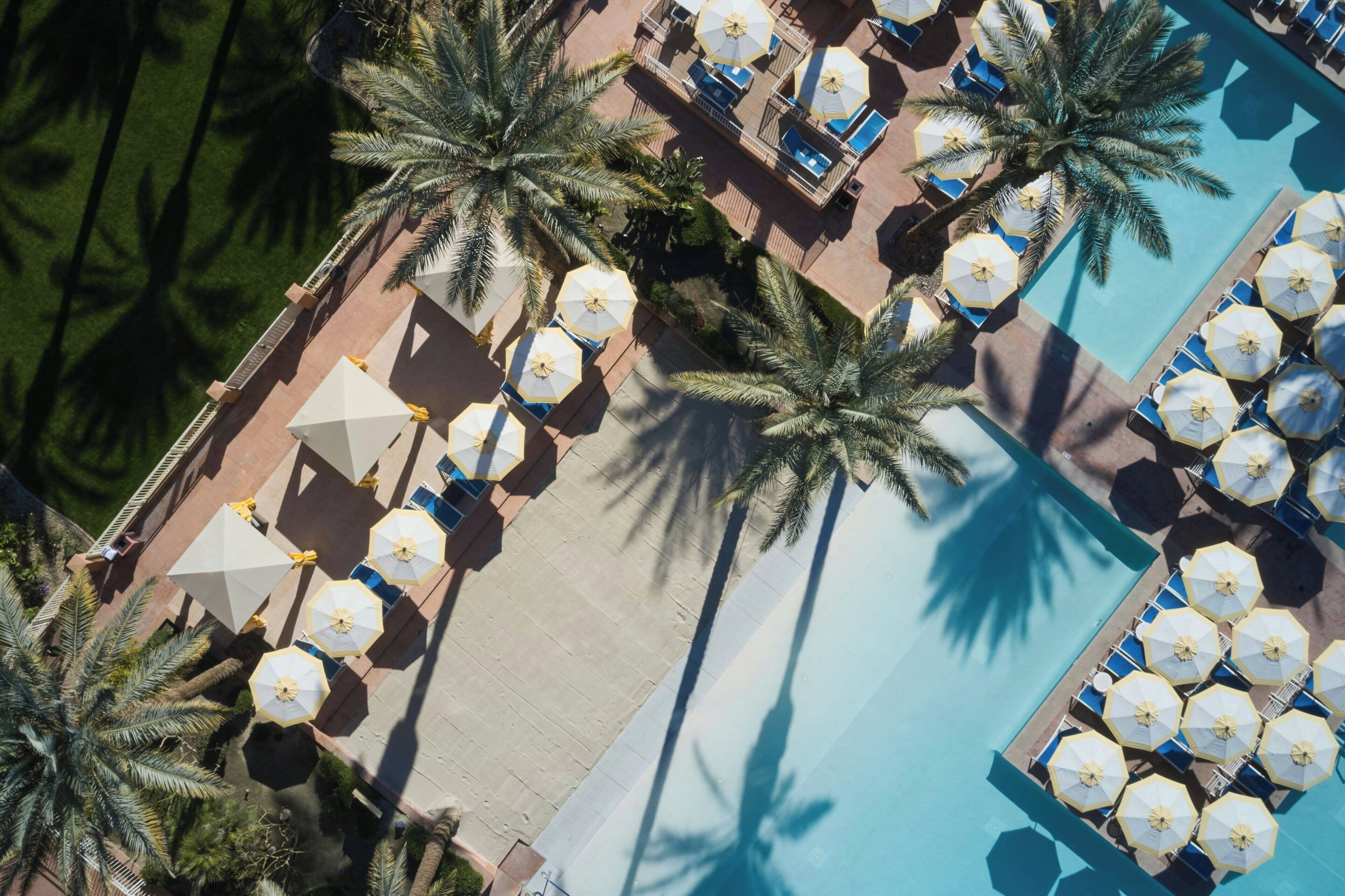 Een luchtendekfoto van een resort met een zwembad, ligbedden en palmbomen.