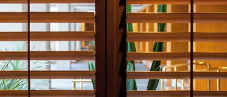 A view through wooden blinds with green plants visible in the background.