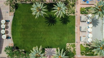 Vista aérea de un resort con un área verde central rodeada de palmeras, mobiliario exterior con sombrillas y una zona de piscina.