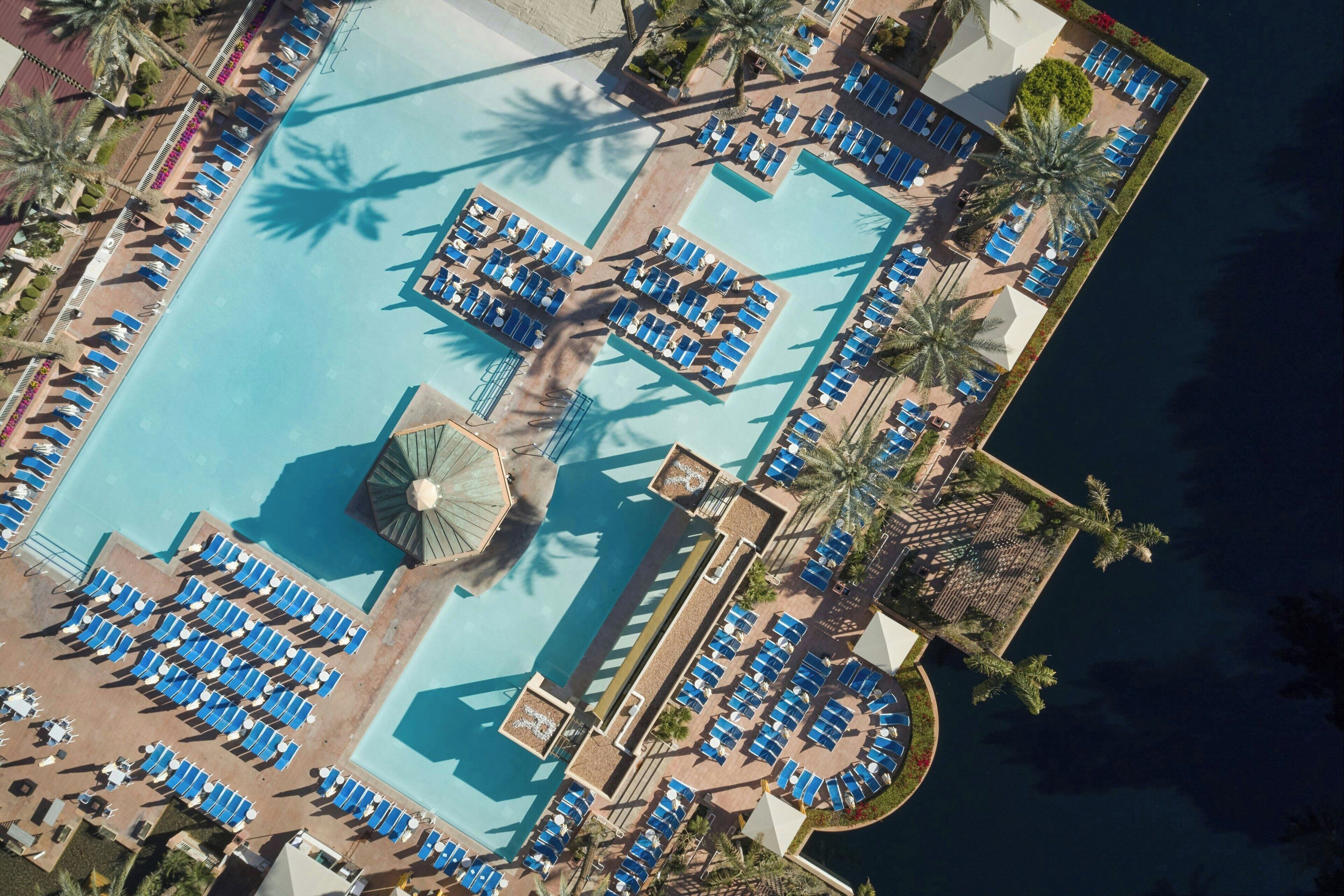 An aerial view of a resort with multiple swimming pools, sun loungers, and palm trees.