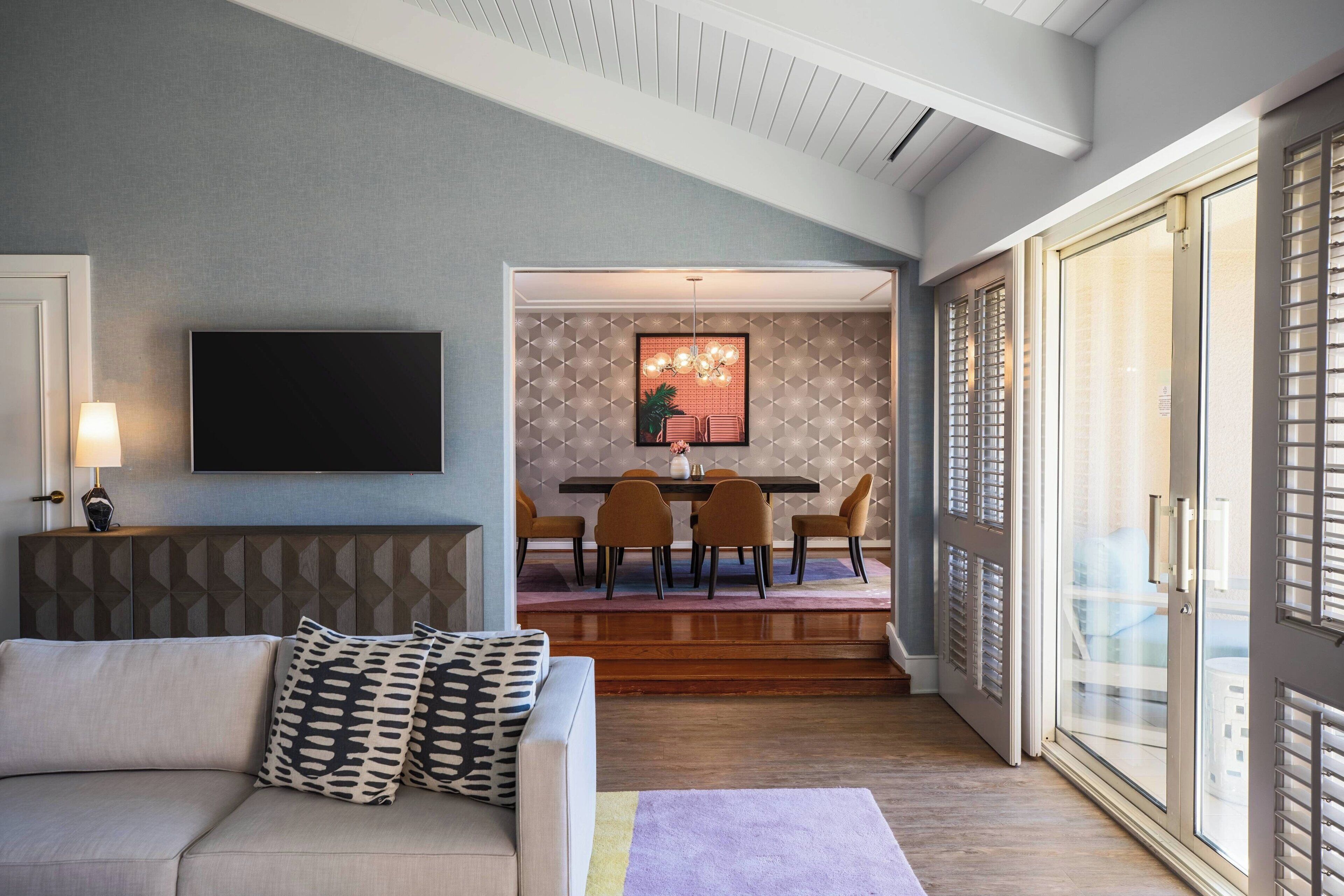 A modern living room with a sofa, a flat-screen TV, and a dining area with a table and chairs.