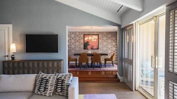 A modern living room with a sofa, a flat-screen TV, and a dining area with a table and chairs.