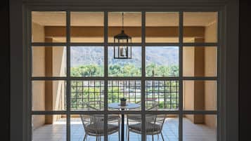 A room with a view through a window with multiple panes, featuring a table with chairs and a hanging light fixture.