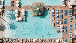 Vue aérienne d’un complexe hôtelier doté d’une piscine centrale, de nombreuses chaises longues et de palmiers.