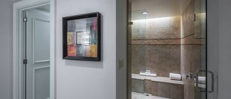 A modern bathroom with a glass shower enclosure, a white door, and a framed artwork on the wall.