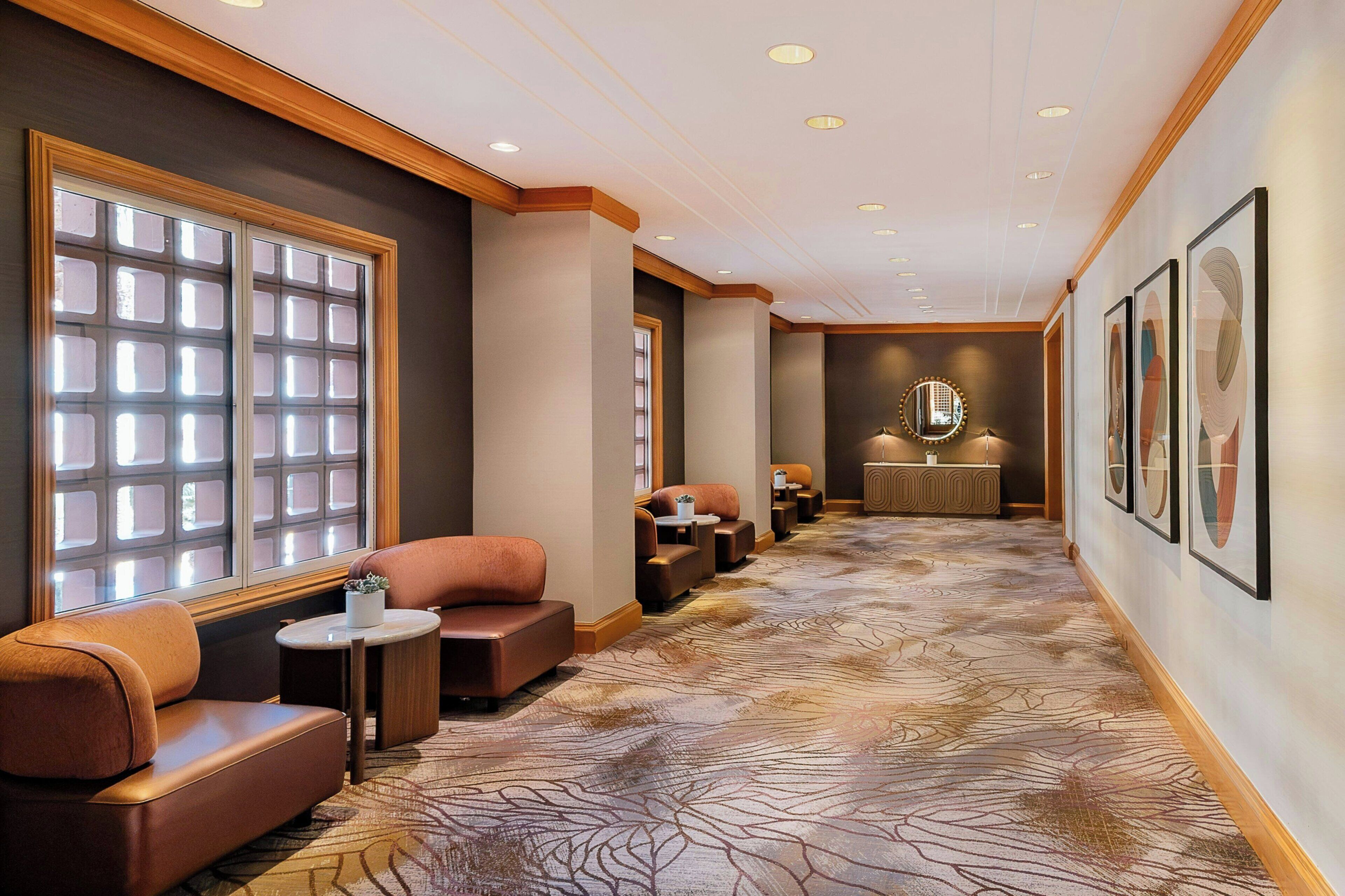 A hotel corridor with seating areas, a reception desk, and framed artwork on the walls.