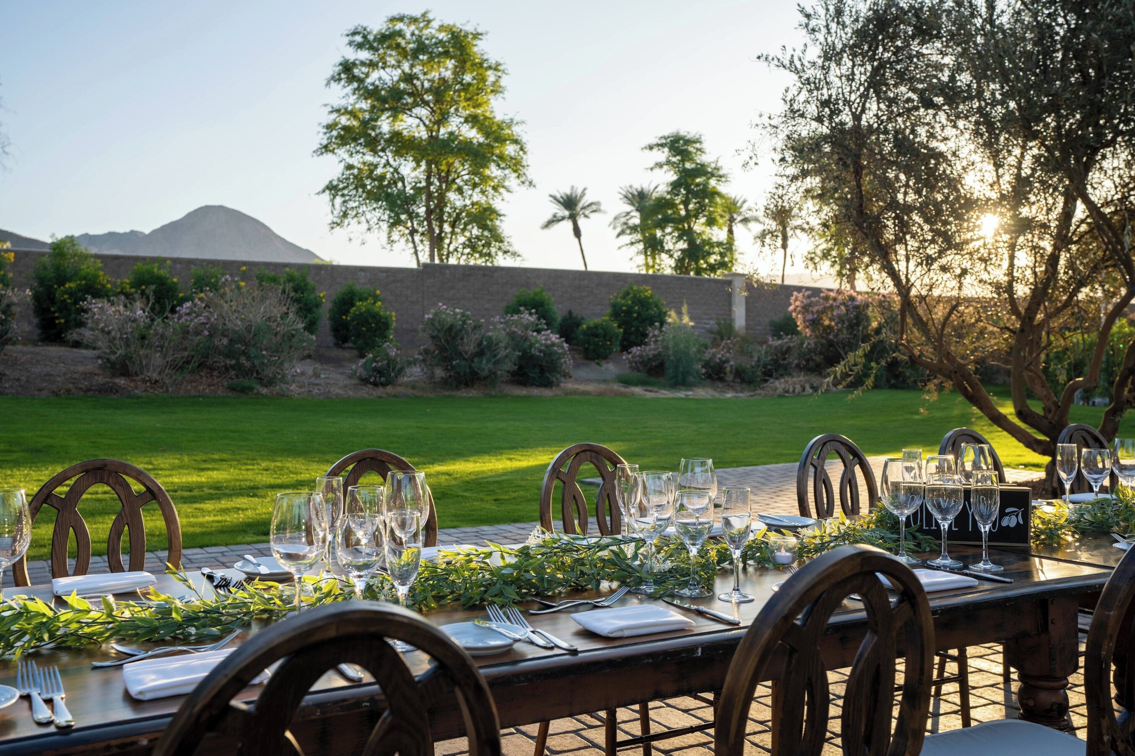 Un espace de restauration en plein air, avec une table dressée pour un repas, entourée de chaises, et offrant une vue sur un paysage verdoyant et des arbres.