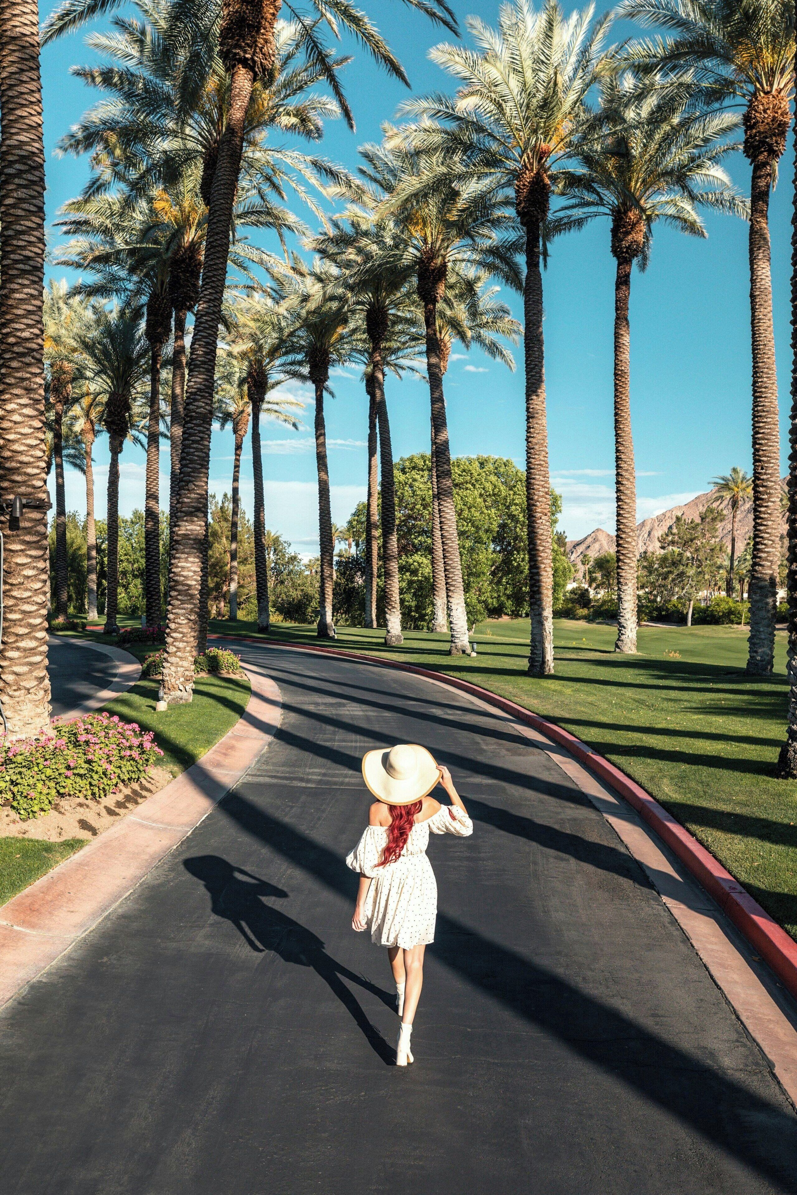 Una mujer caminando por un camino bordeado de palmeras.